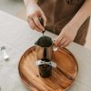 Close-up of a person making candles with metal cup and tools on a wooden tray.