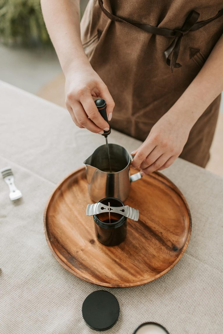 Close-up of a person making candles with metal cup and tools on a wooden tray.