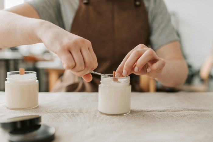 Photo by Vlada Karpovich Close-up of artisan crafting handmade candles with wooden wicks in workshop.