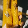 Close-up of handcrafted yellow beeswax candles with floral decorations, held in hand, showcasing intricate texture.