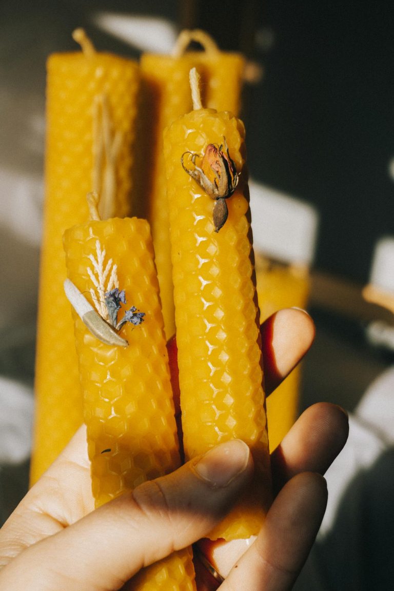 Close-up of handcrafted yellow beeswax candles with floral decorations, held in hand, showcasing intricate texture.