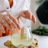 Hands crafting a wooden wick candle in a glass jar on a natural wooden base, reflecting handmade artisan work.