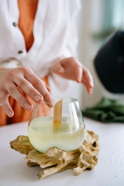 Hands crafting a wooden wick candle in a glass jar on a natural wooden base, reflecting handmade artisan work.